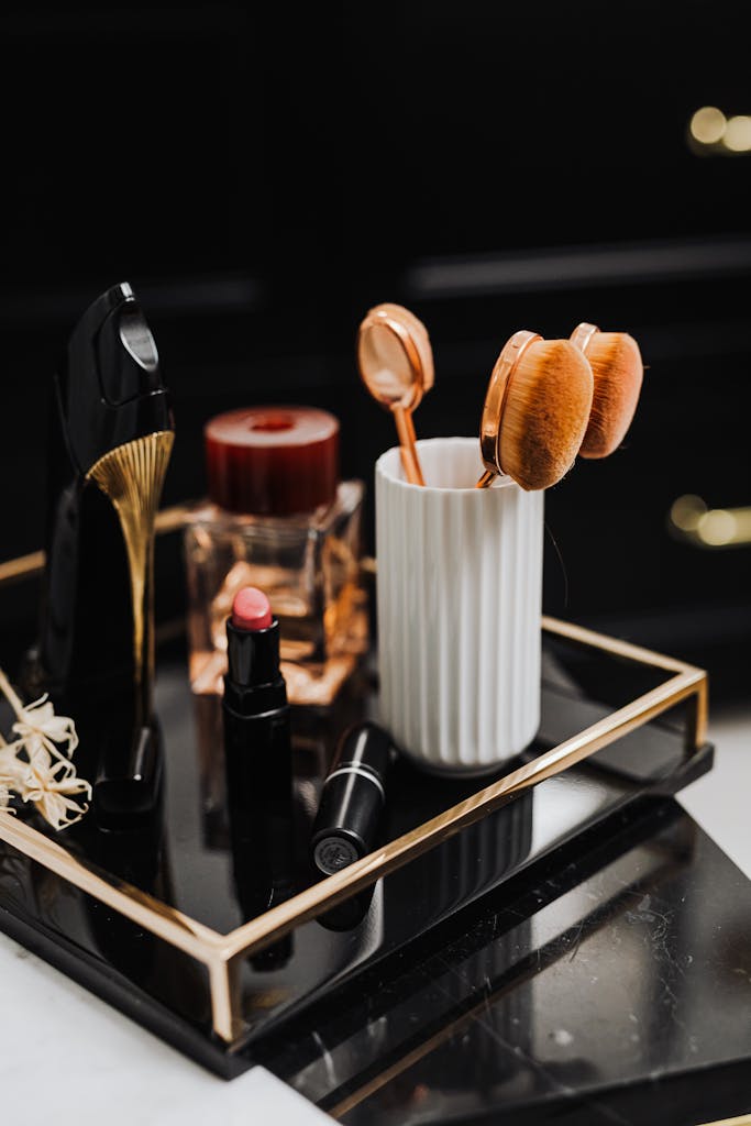 A stylish display of makeup and beauty tools including lipstick, brushes, and perfume on a black tray.