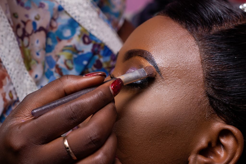 Close-up image of a makeup artist applying eyeshadow to a woman's eyelid, highlighting beauty and fashion.