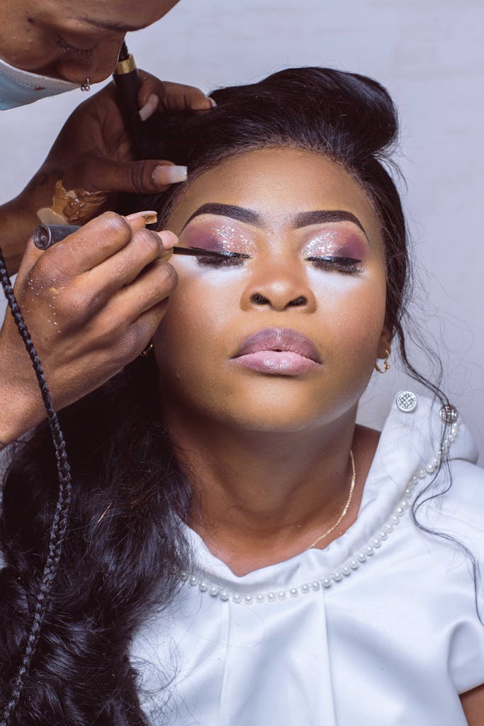 Close-up of a woman receiving eye makeup by a professional makeup artist, emphasizing fashion and beauty.