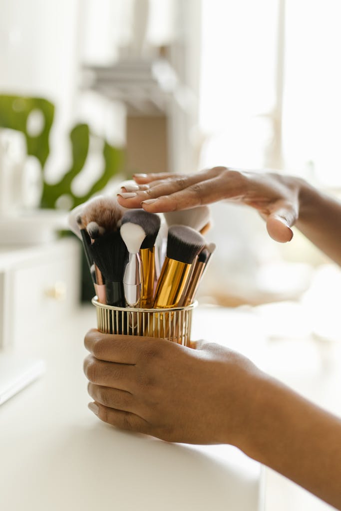 Close-up of hands organizing various makeup brushes in a stylish container, captured indoors.