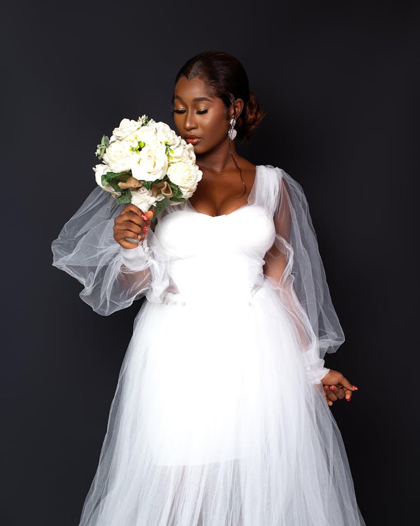 Elegant African bride holding a bouquet on a black background, showcasing wedding fashion.
