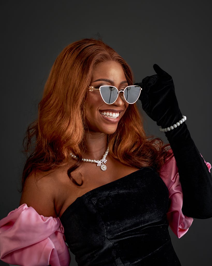 Stylish woman smiling in sunglasses, pearls, and gloves. Elegant fashion portrait.